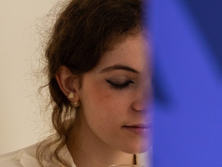 Femme avec des cheveux bouclés, regard pensif de profil, partiellement cachée par un objet.