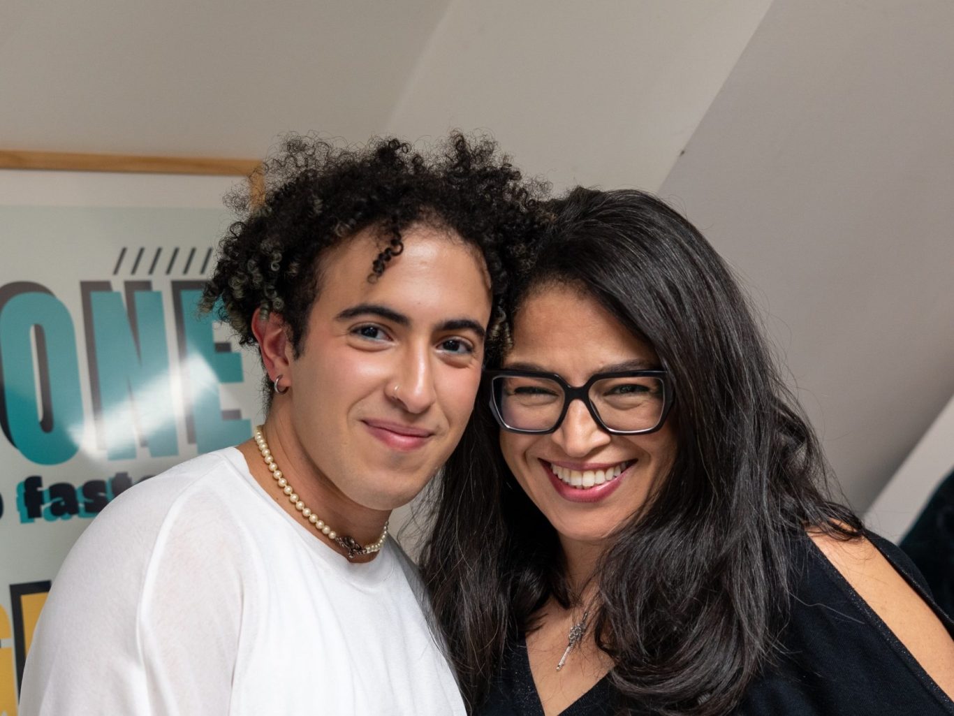 Deux personnes souriantes posent ensemble, l'une avec des cheveux bouclés, l'autre avec des lunettes.