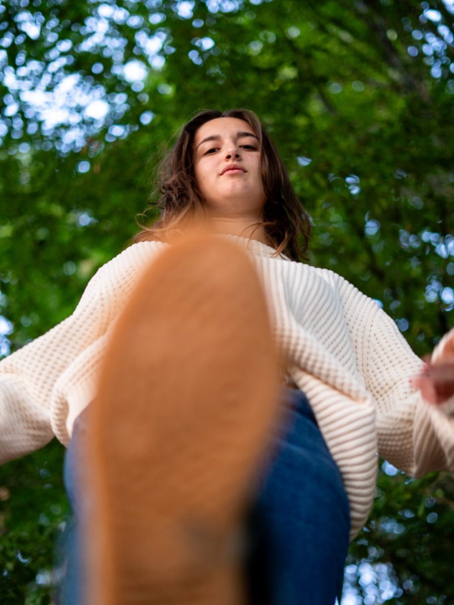 Femme en pull blanc, vue de bas, avec des arbres en arrière-plan.