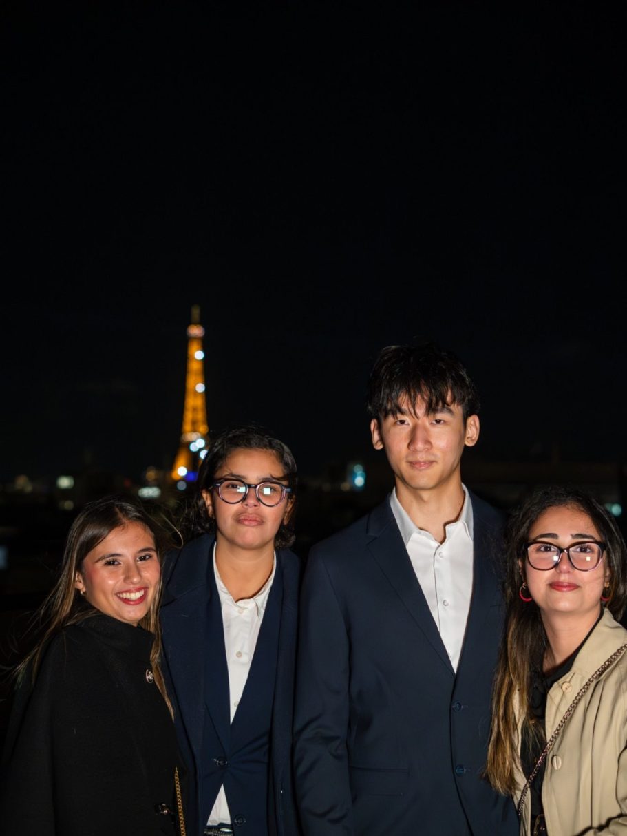 Quatre personnes souriantes devant la tour Eiffel illuminée, nuit claire.