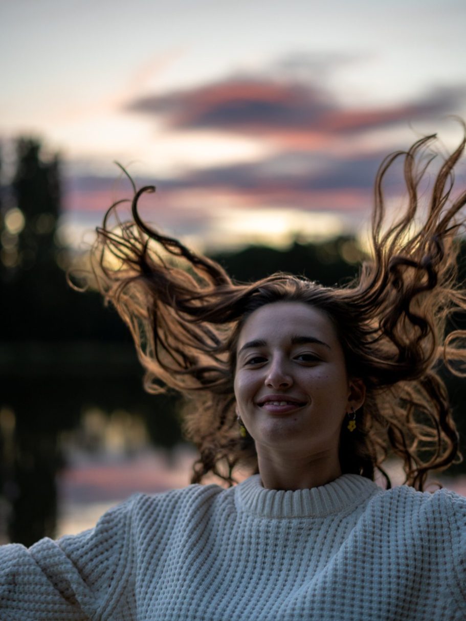 Femme souriante avec des cheveux flottants sur fond de coucher de soleil au bord de l'eau.