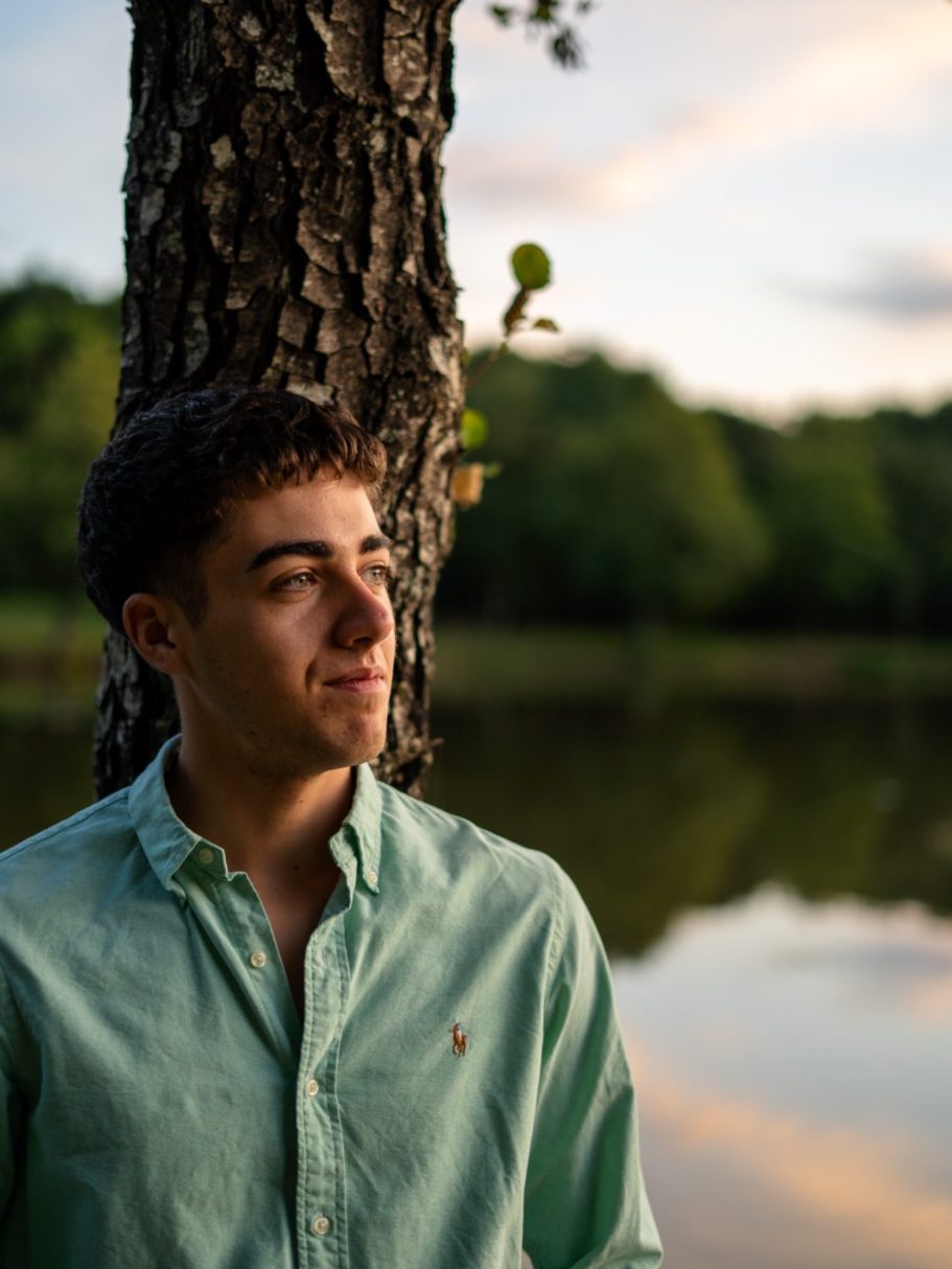 Un jeune homme en chemise verte, pensif, près d'un lac au coucher du soleil.