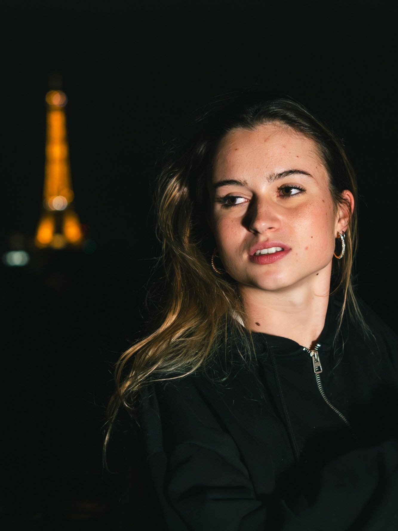 Jeune femme avec des cheveux longs et blonds, fond de la Tour Eiffel illuminée.