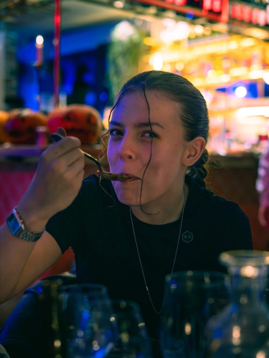 Une jeune femme dégustant un plat, regard pensif, ambiance lumineuse en arrière-plan.