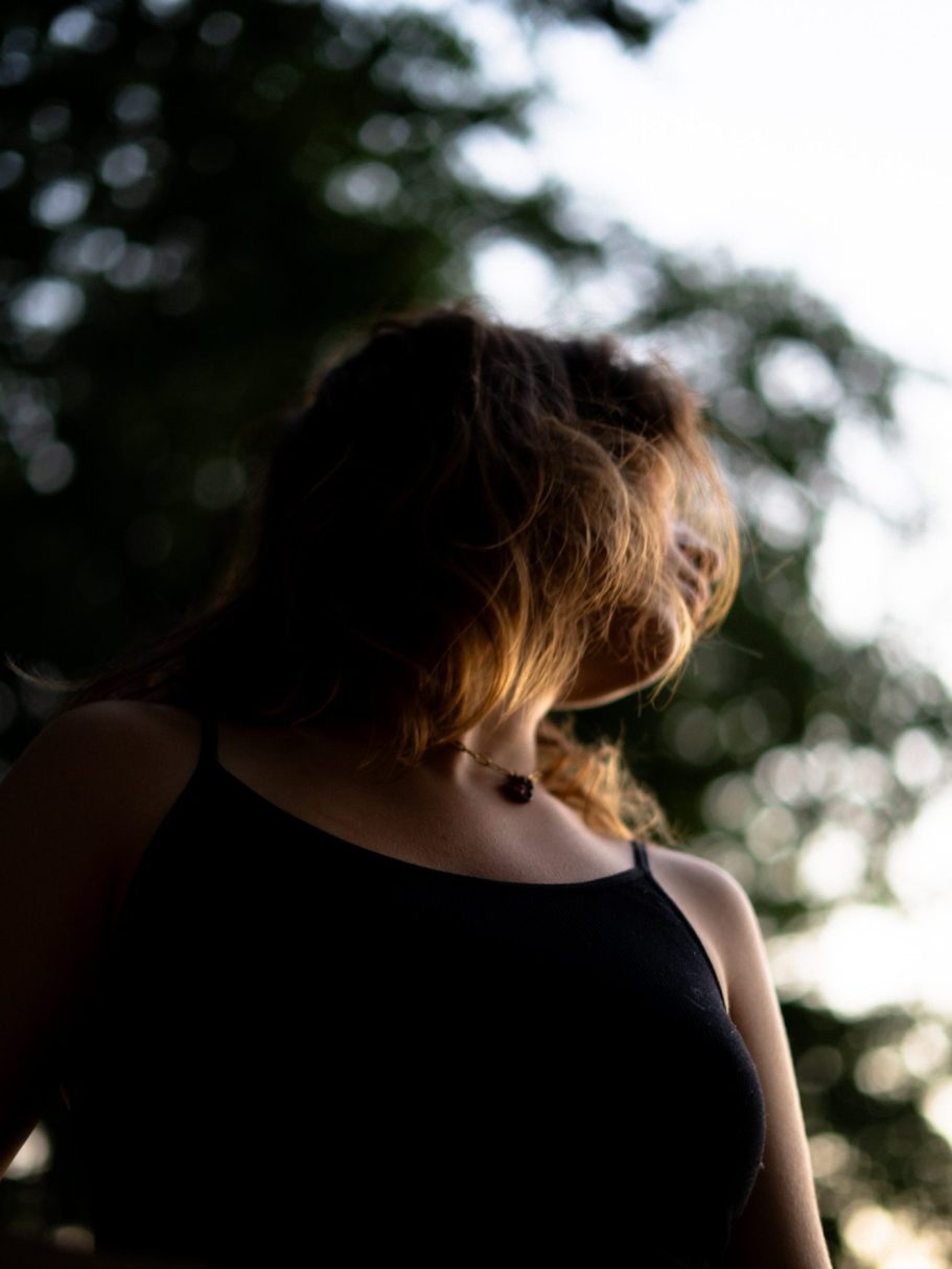 Une silhouette féminine de dos, cheveux au vent, avec un ciel lumineux en arrière-plan.