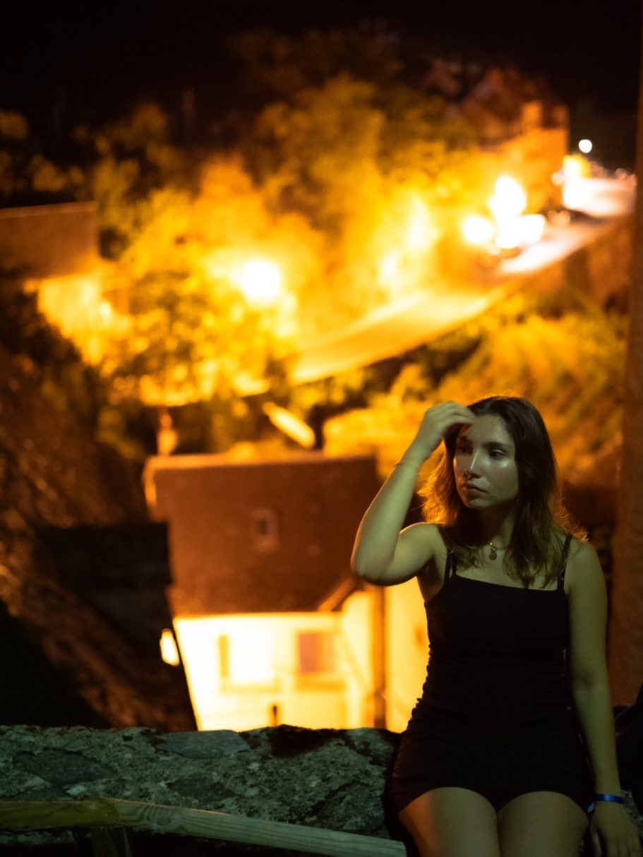 Femme pensant, vêtue en noir, avec des lumières orange et jaunes en arrière-plan.
