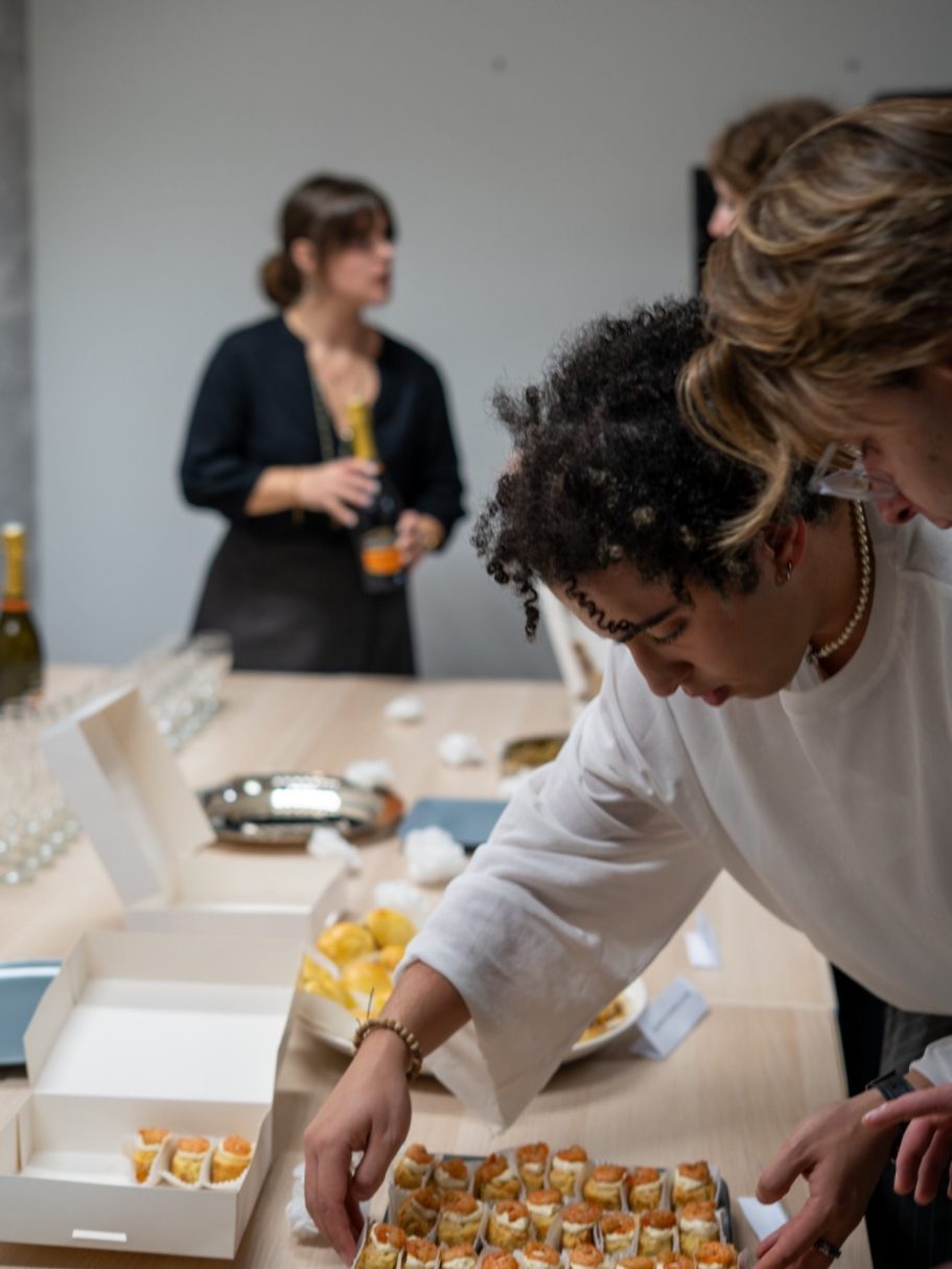 Une personne prépare des bouchées apéritives pendant un événement, avec des convives en arrière-plan.