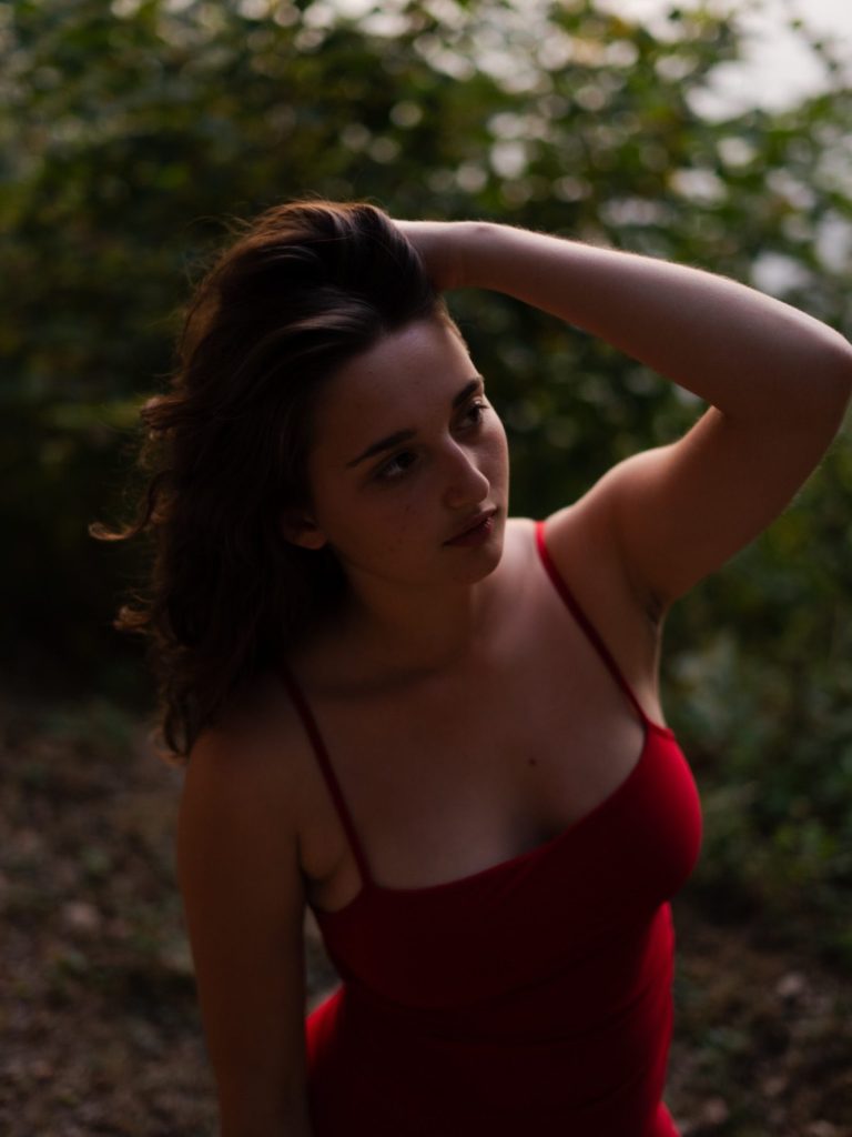 Jeune femme en robe rouge, posant au milieu d'une nature verdoyante.