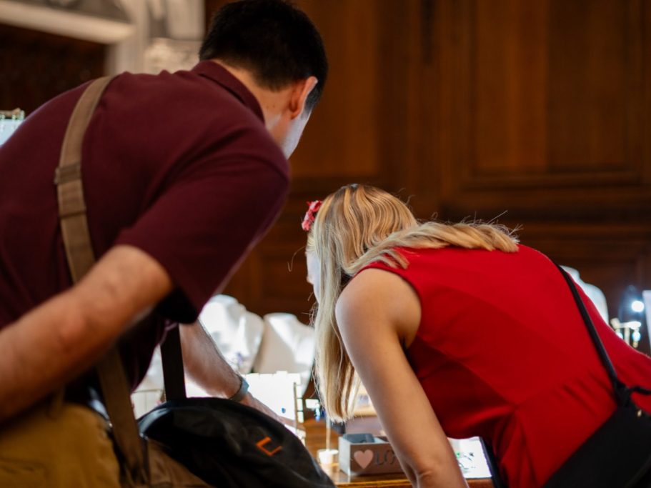 Deux personnes examinant de près des objets sur une table, l'une en rouge et l'autre en violet.
