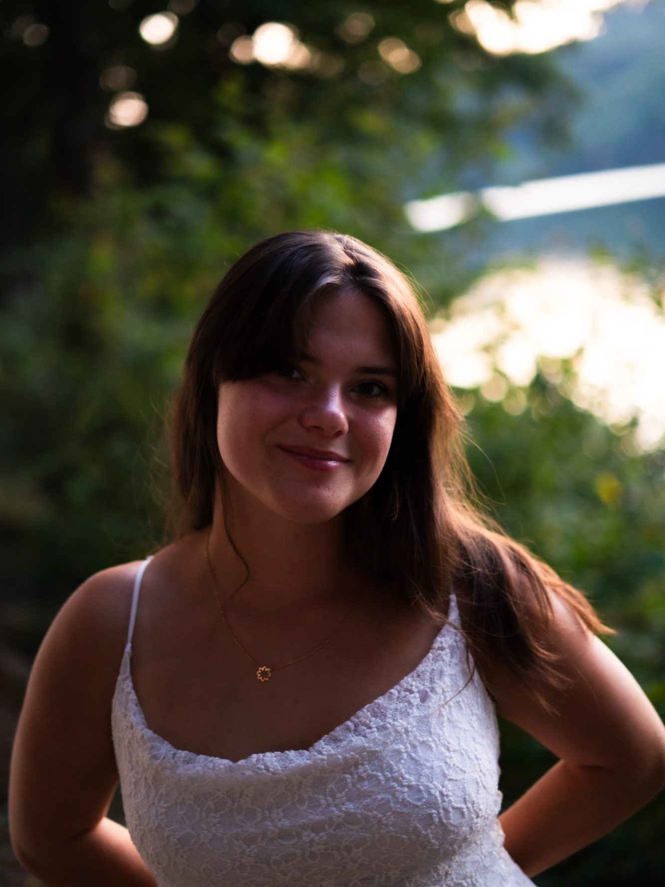 Portrait d'une jeune femme souriante, avec des cheveux bruns, devant un paysage verdoyant.