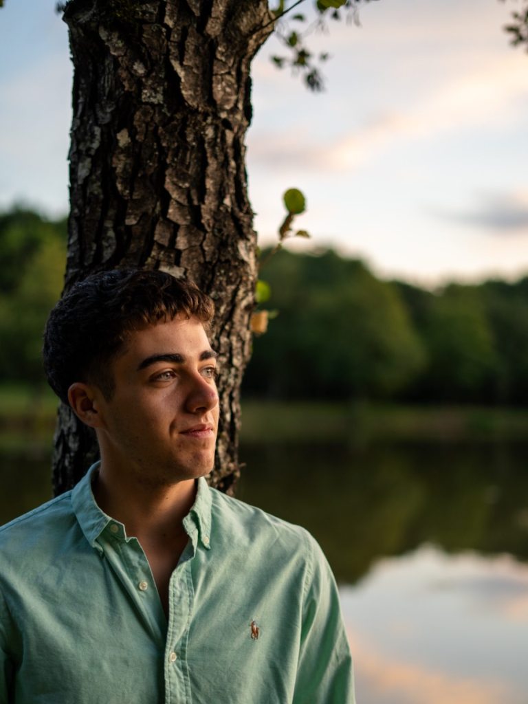 Jeune homme avec une chemise verte, posé près d'un arbre au bord d'un lac.