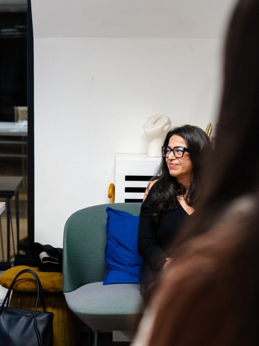 Jeune femme souriante avec des lunettes assise sur un canapé, à l’ambiance décontractée.