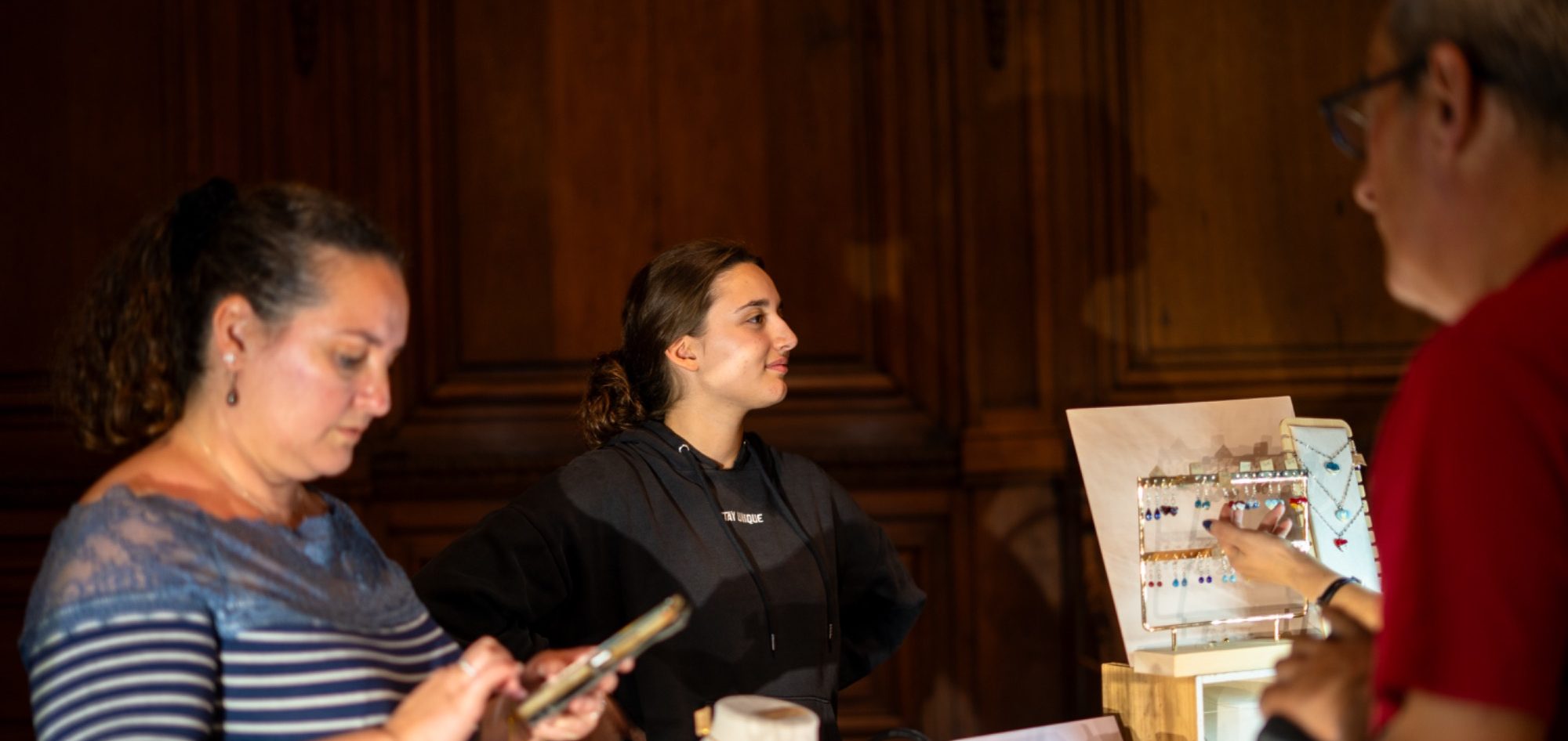 Trois personnes discutent dans un espace sombre, avec un tableau d'affichage en arrière-plan.