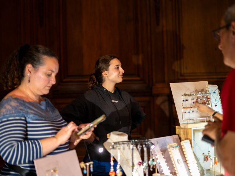 Deux personnes discutent près d'un stand de bijoux, l'une utilisant son téléphone.
