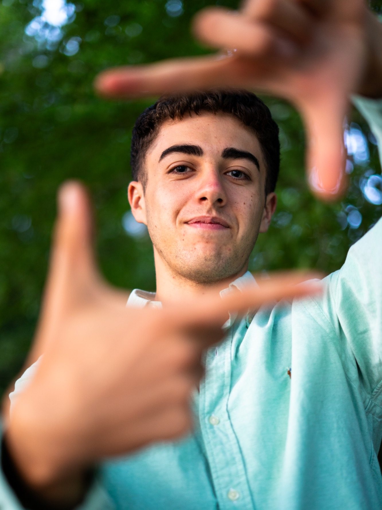 Jeune homme souriant formant un cadre avec ses mains devant un arrière-plan flou.