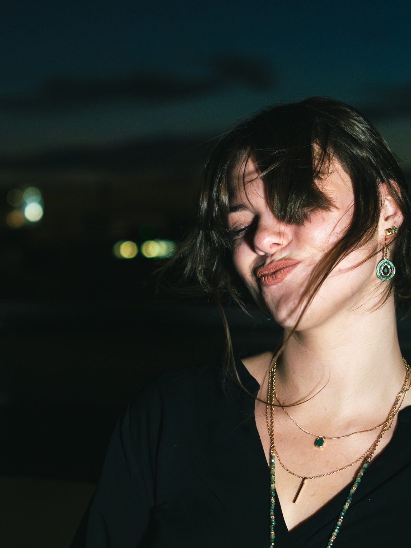 Femme souriante avec des cheveux au vent, à l'arrière-plan nocturne flou.