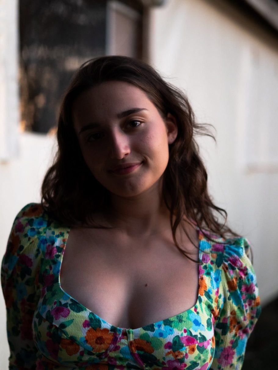 Jeune femme souriante avec des fleurs colorées sur une robe, en arrière-plan flou.