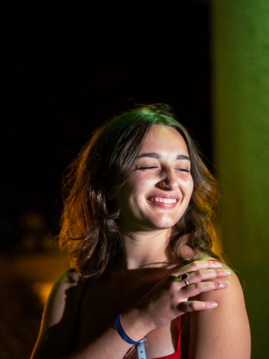 Femme souriante avec les cheveux ondulés, se tenant sous une lumière douce.