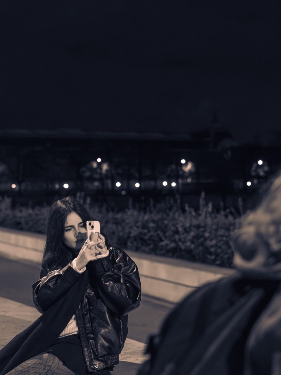 Femme assise dans un parc sombre, prenant une photo avec son téléphone.
