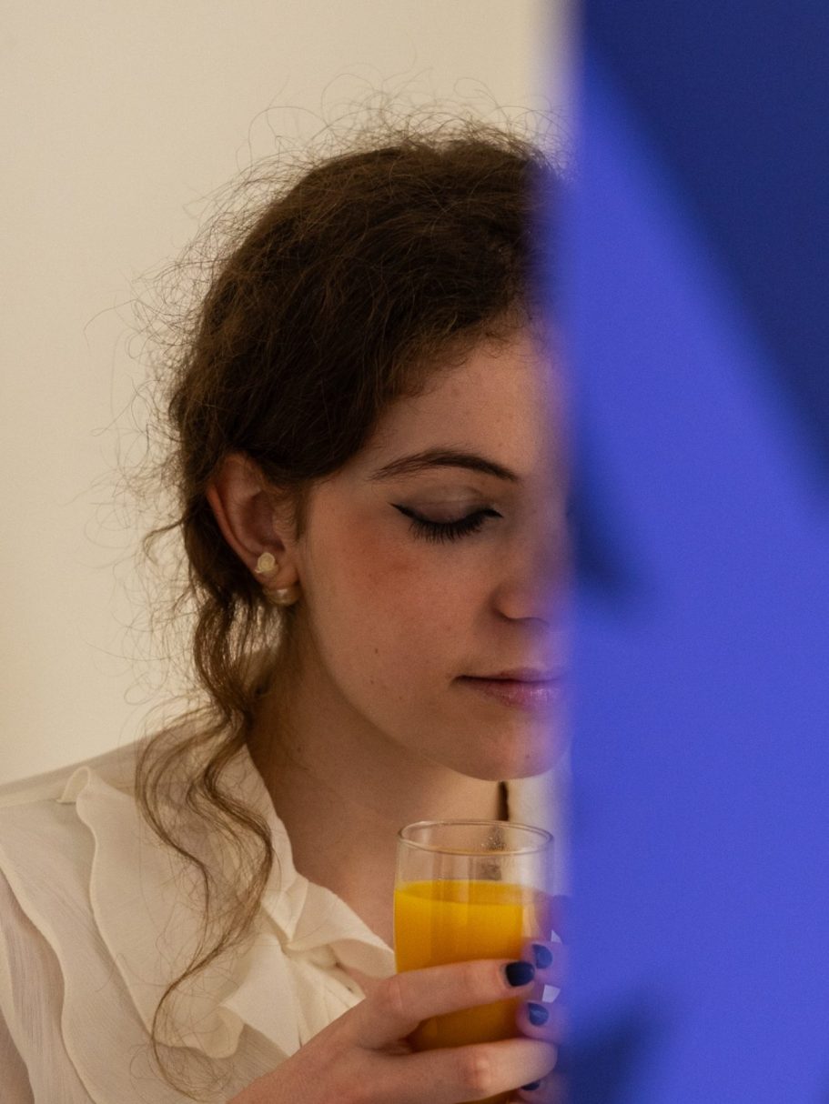 Femme avec un verre de jus, légèrement floue, un mur bleu en arrière-plan.