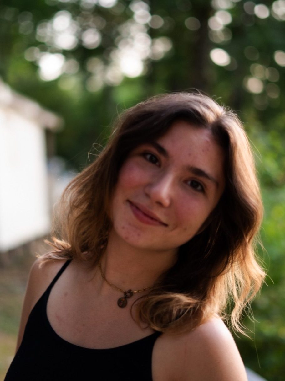 Femme souriante avec des cheveux ondulés, portant un débardeur, en arrière-plan verdoyant.