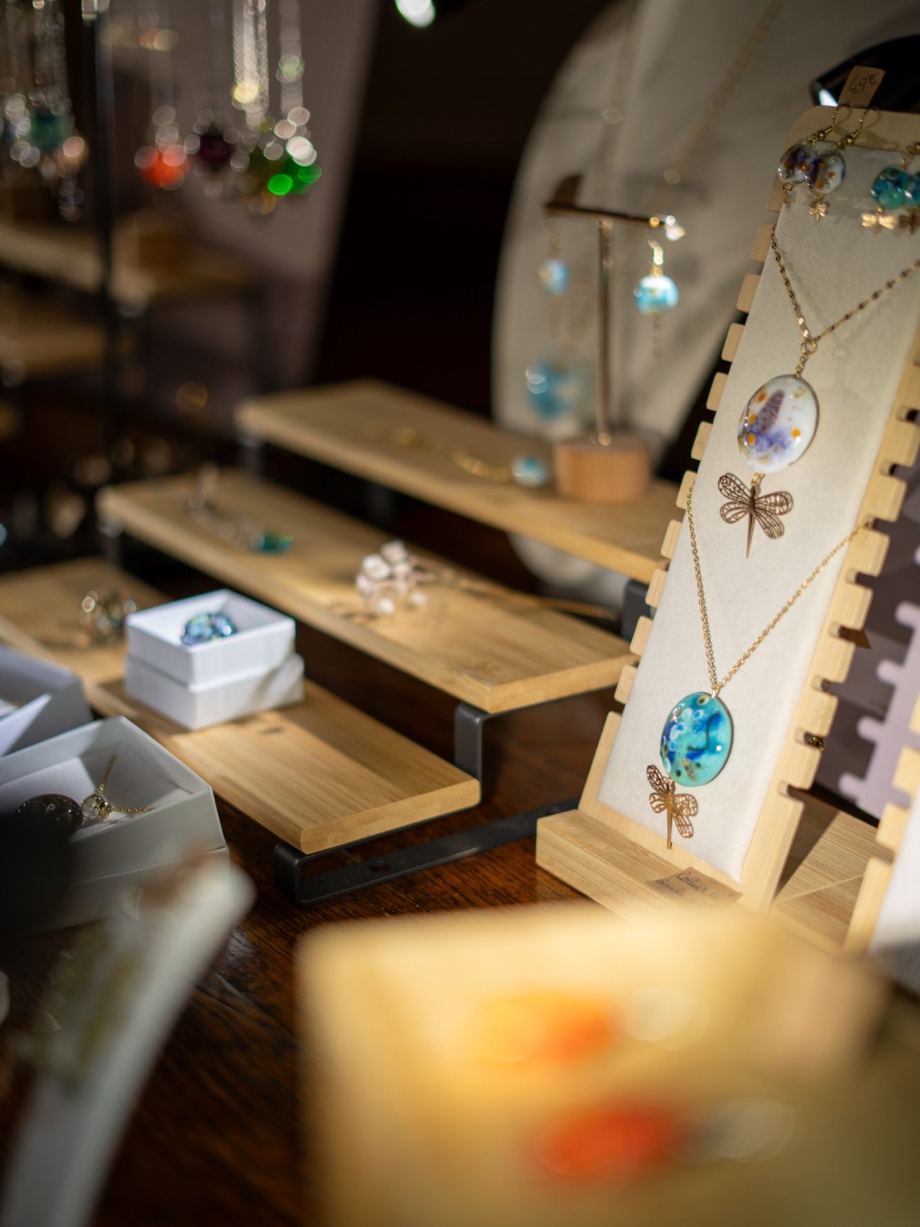 Bijoux artisanaux exposés sur des supports en bois, avec des décorations colorées.