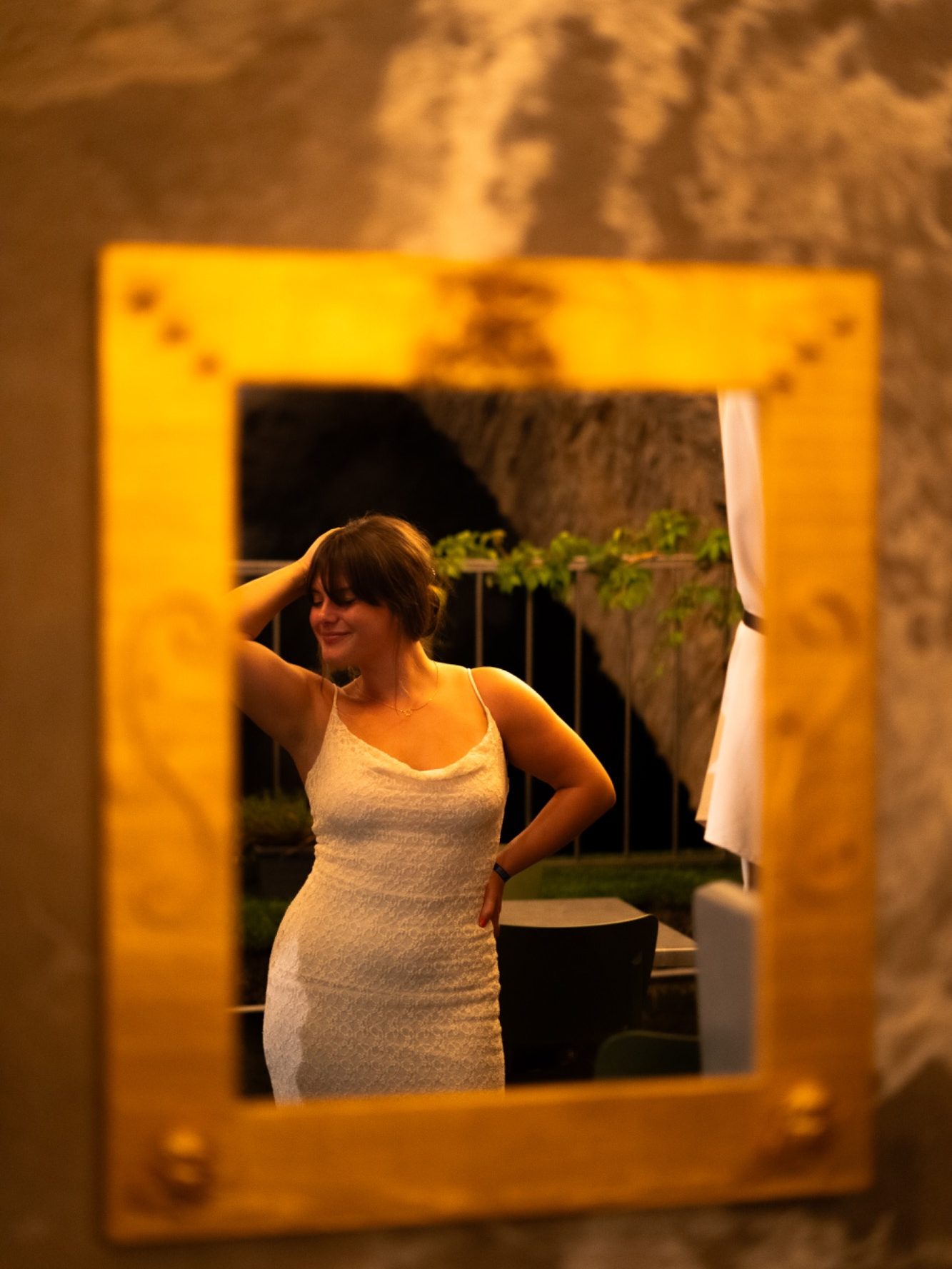 Femme en robe blanche posant devant un miroir avec un cadre doré.