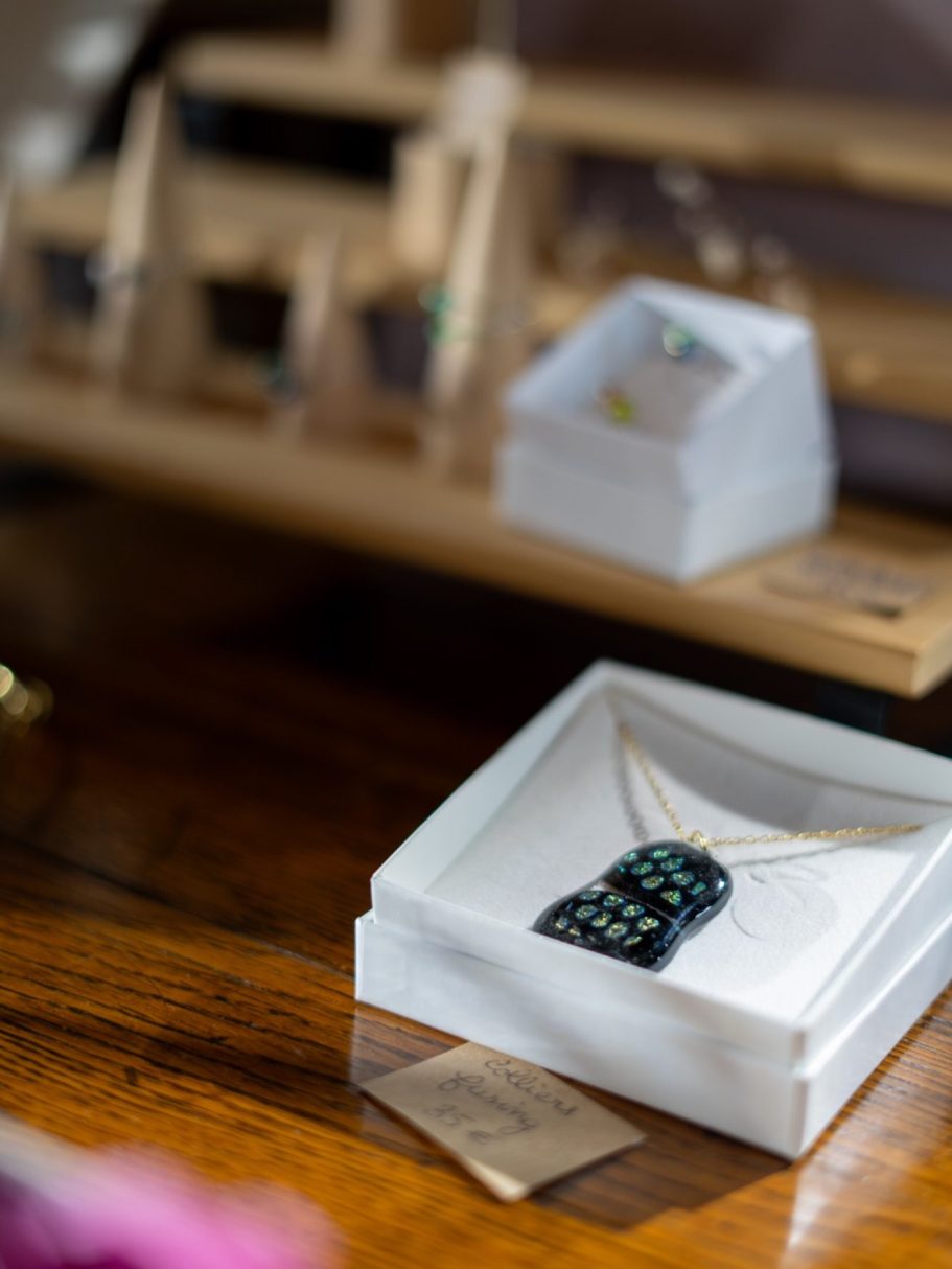 Collier délicat dans une boîte blanche, avec des bijoux en arrière-plan.