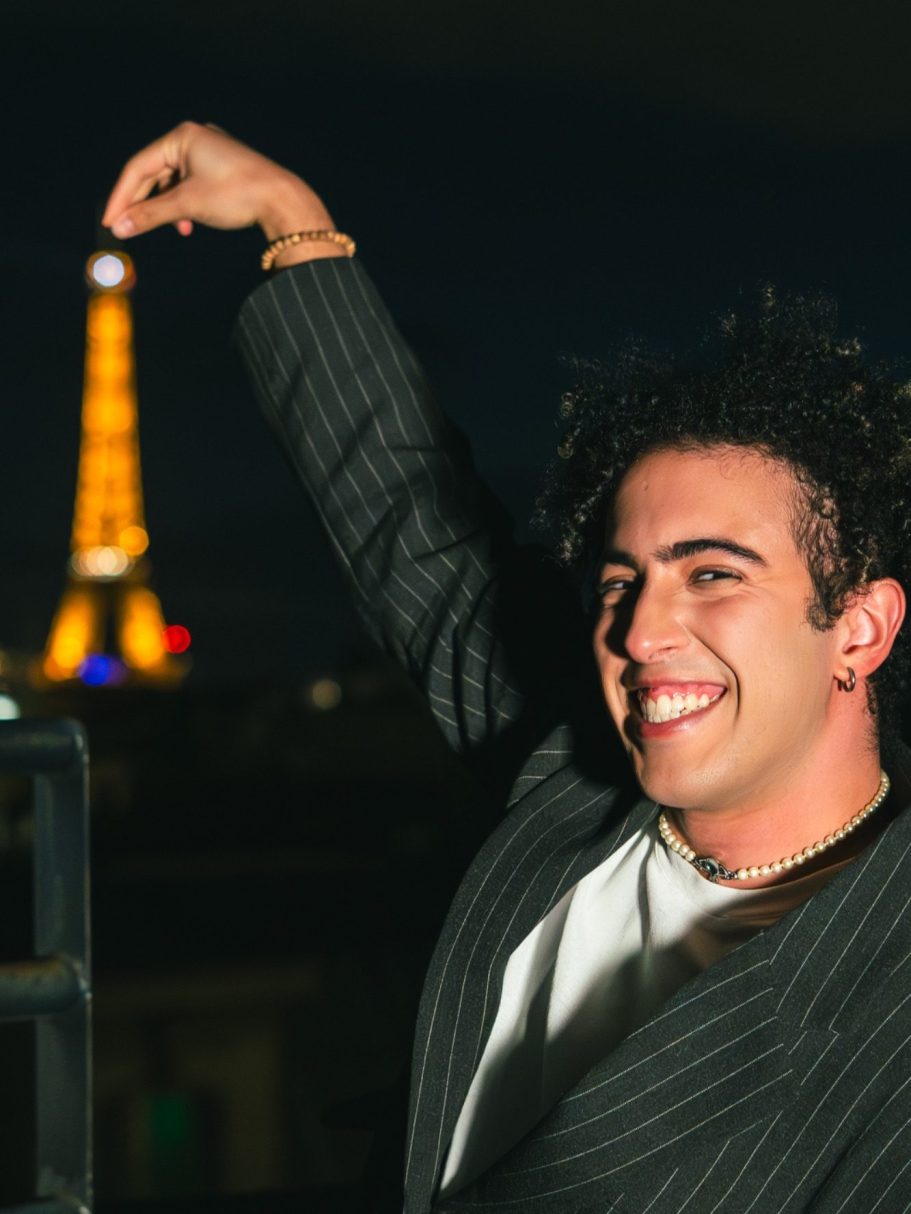 Un homme souriant tient la tour Eiffel en miniature, illuminée en arrière-plan.