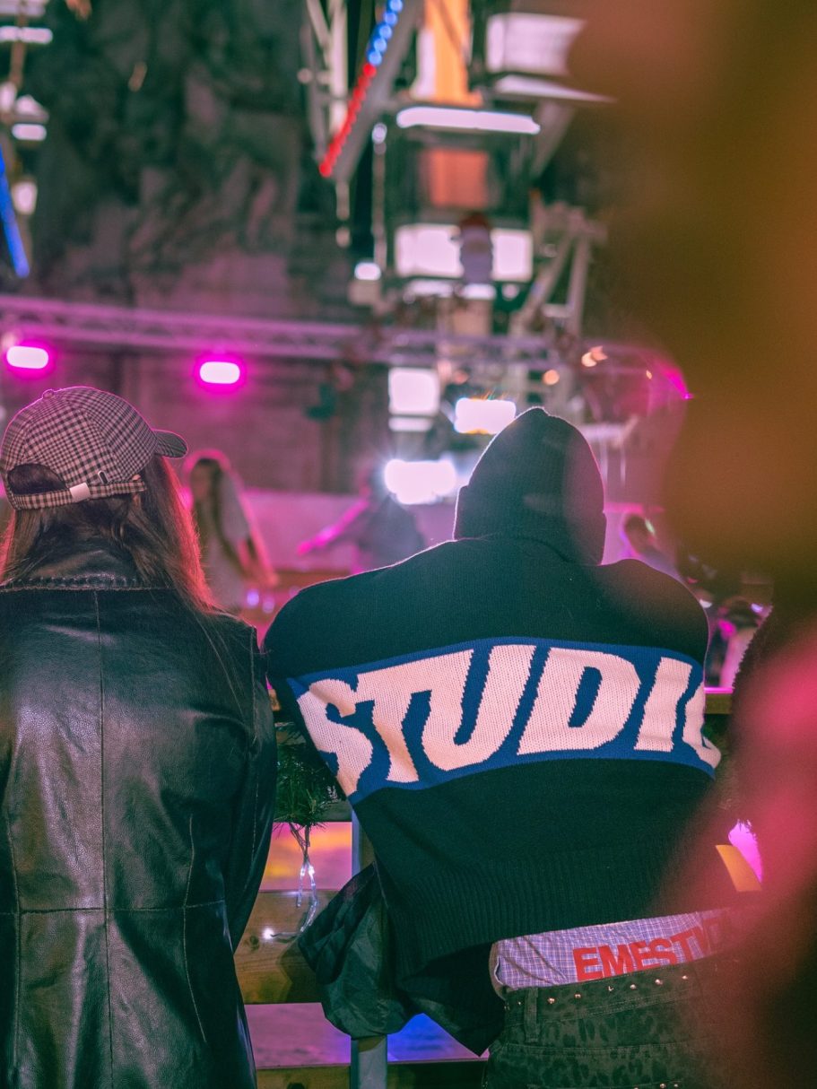 Deux personnes regardent un spectacle en soirée, lumières colorées en arrière-plan.
