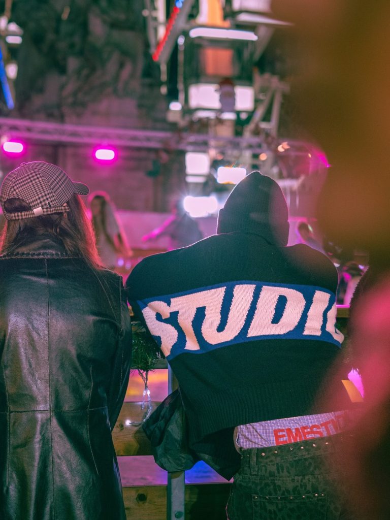 Personnes de dos dans un environnement festif, avec des éclairages colorés et un gros plan sur un sweat à capuche.