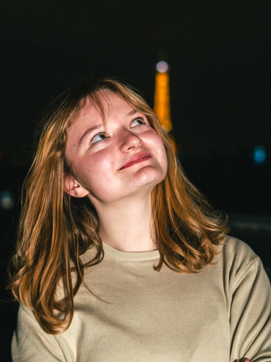 Jeune femme aux cheveux châtains, regardant vers le ciel avec la Tour Eiffel en arrière-plan.