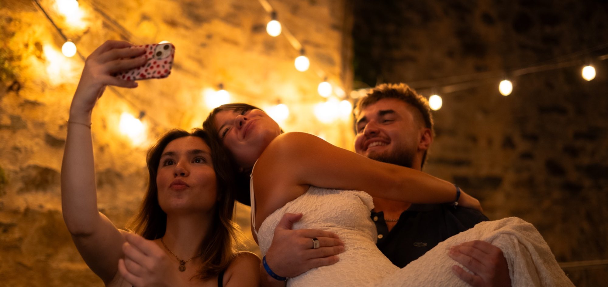 Trois personnes prennent un selfie dans une ambiance lumineuse et festive.