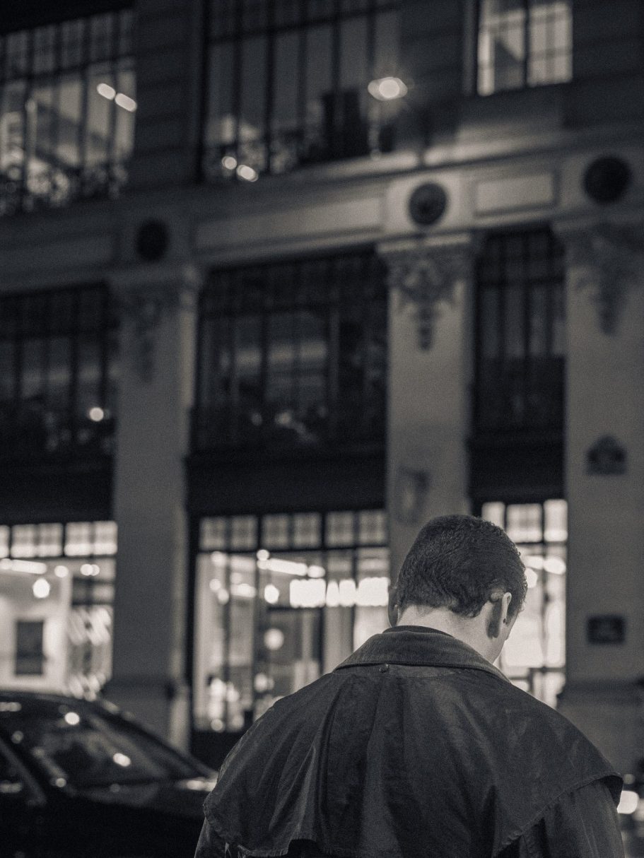 Homme de dos, regardant son téléphone devant un bâtiment éclairé la nuit.