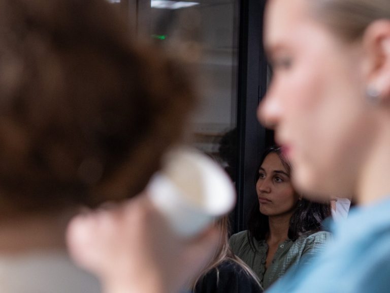 Deux femmes sont présentes, l'une tenant une tasse et l'autre observant au fond.
