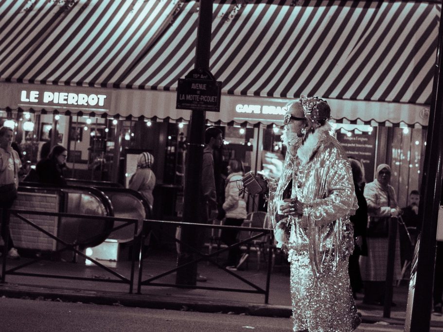 Personne en habit brillant dans une rue animée, avec des parasols en arrière-plan.