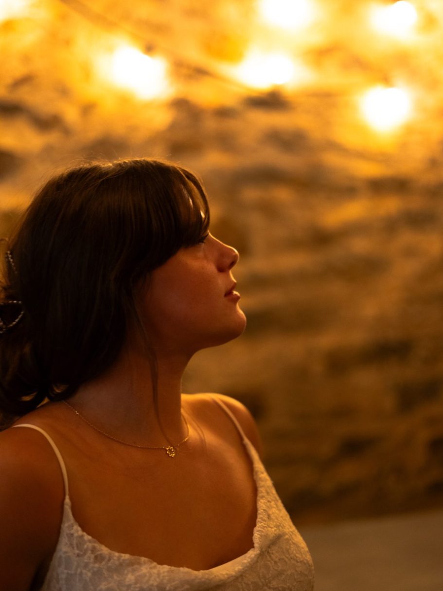 Femme de profil sous une lumière douce, avec un fond en pierre.