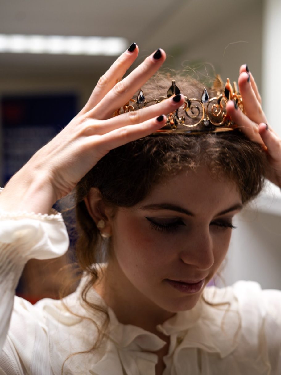 Femme portant une couronne avec les mains, vêtue d'une blouse élégante.