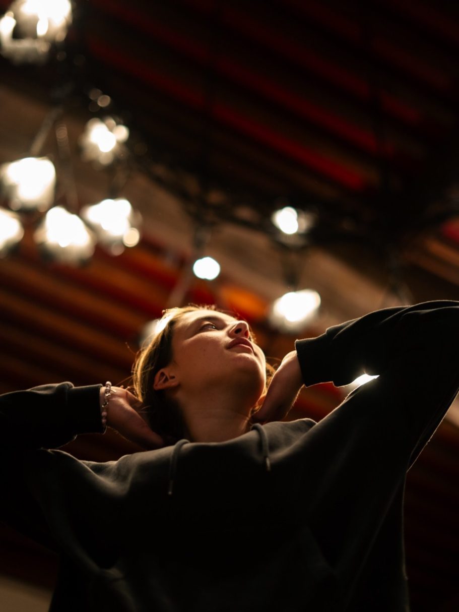 Une personne debout, les mains derrière la tête, regardant vers le haut sous des lumières.