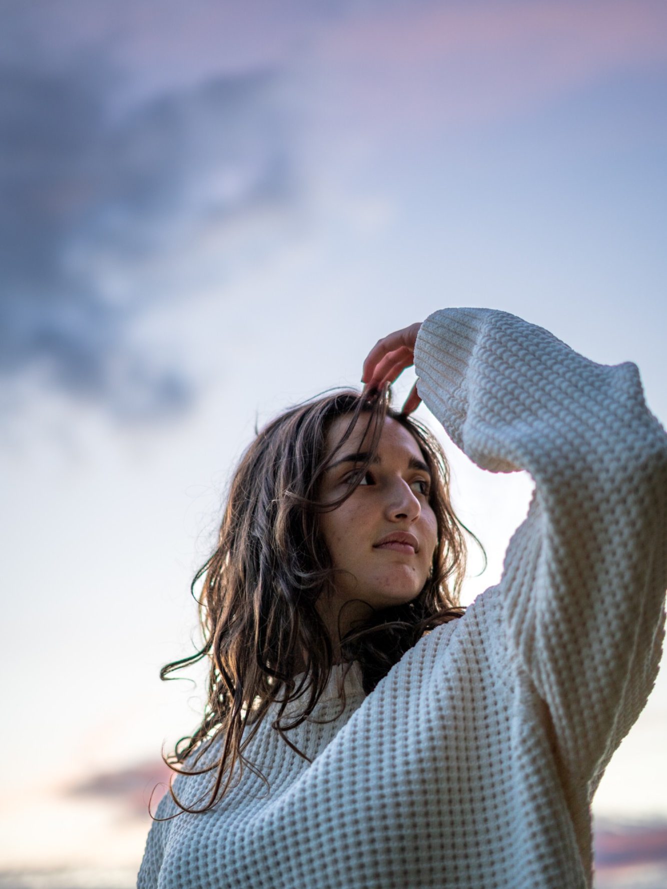 Femme avec un pull surdimensionné, regardant au loin sous un ciel nuageux.