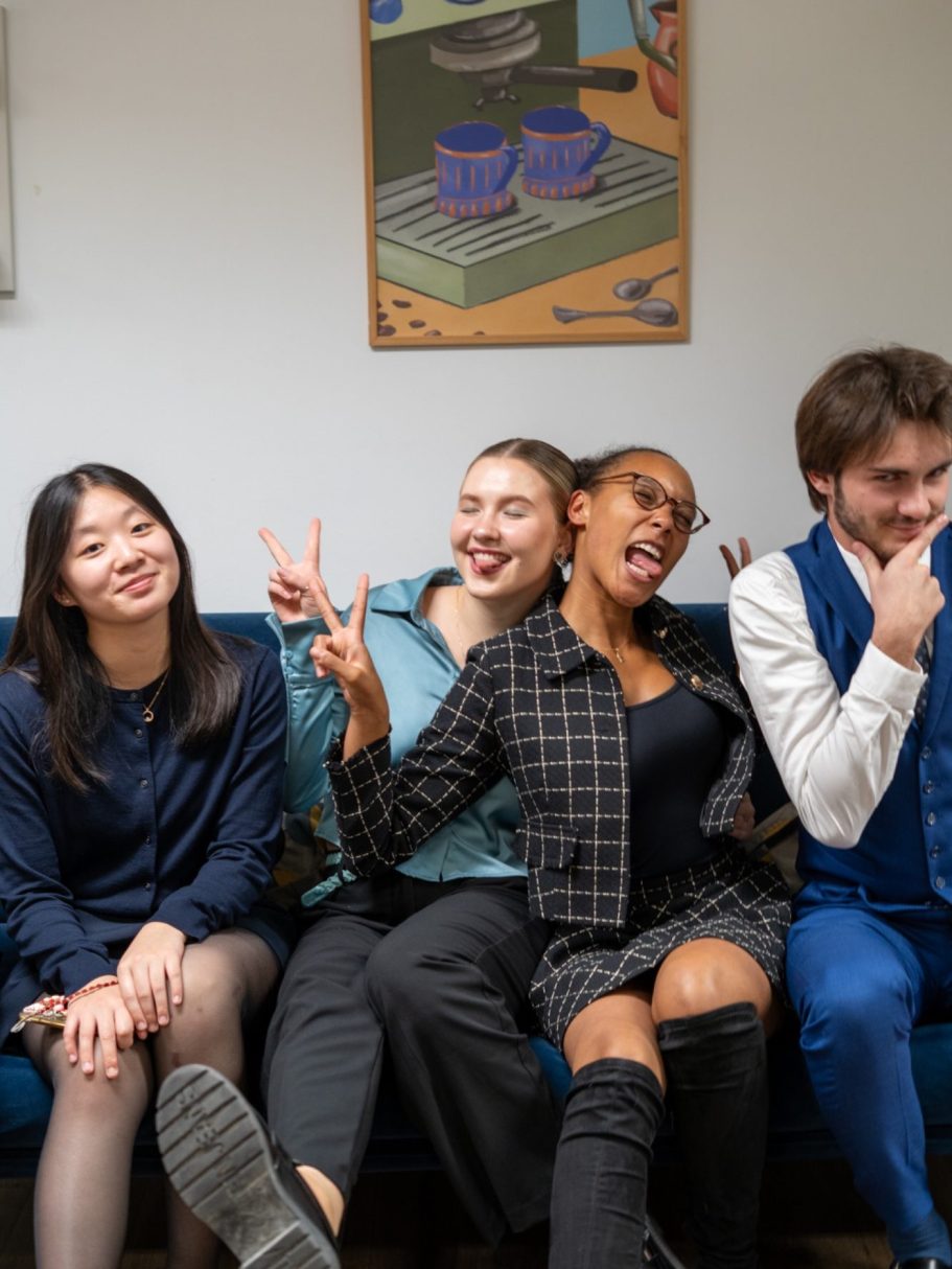 Quatre personnes souriantes posent ensemble, deux faisant des gestes amusants.