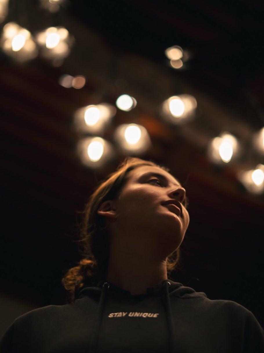 Portrait d'une personne en hoodie, regardant vers le haut avec des lumières floues en arrière-plan.