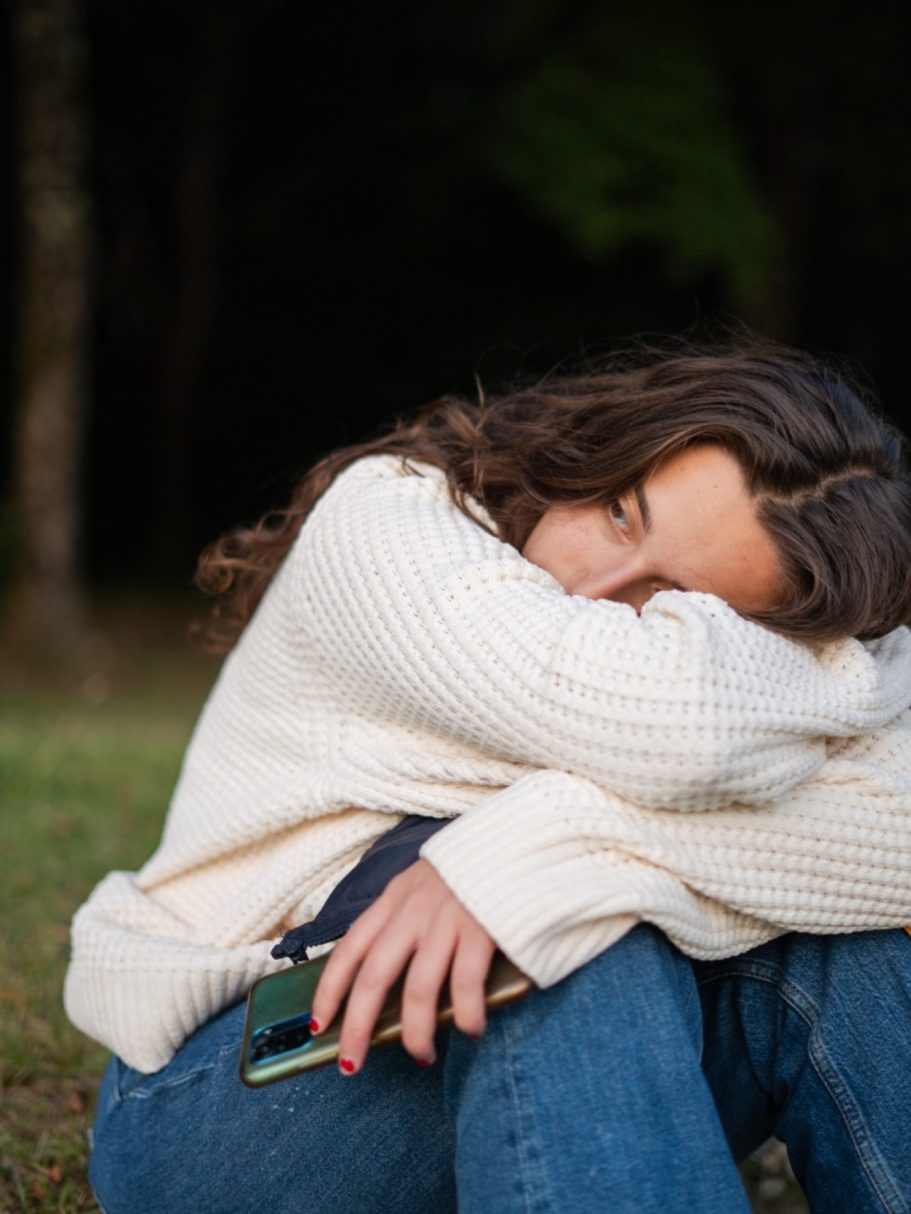 Jeune femme assise sur l'herbe, tête appuyée sur les bras, vêtue d'un pull blanc.