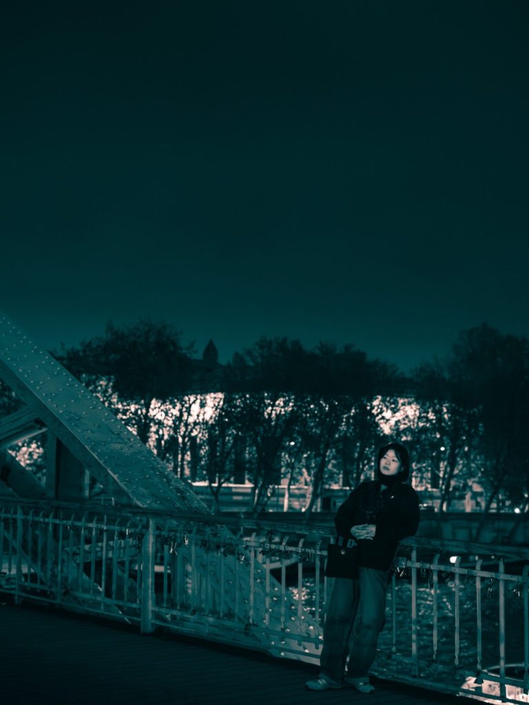 Person debout sur un pont, entouré d'arbres, à la tombée de la nuit.