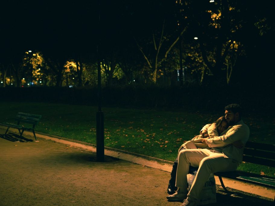 Deux personnes assises sur un banc dans un parc sombre, entourées d'arbres illuminés.
